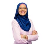 Headshot of Dr Maha Kobeil. Smiling woman wearing a light pink top and a blue hijab against a white background