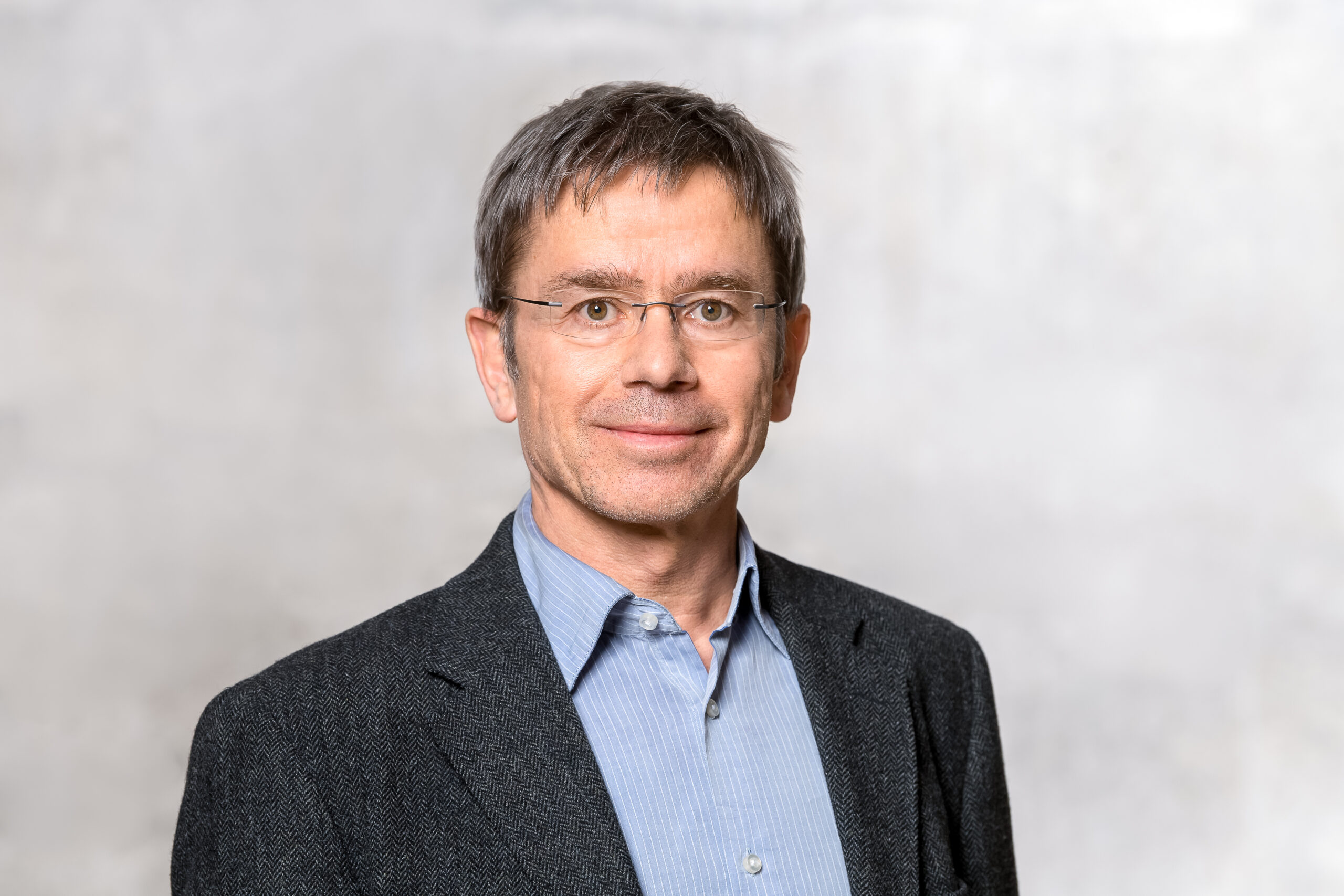 Photo of Prof Stefan Rahmstorf wearing a dark suit and a blue shirt against a grey background